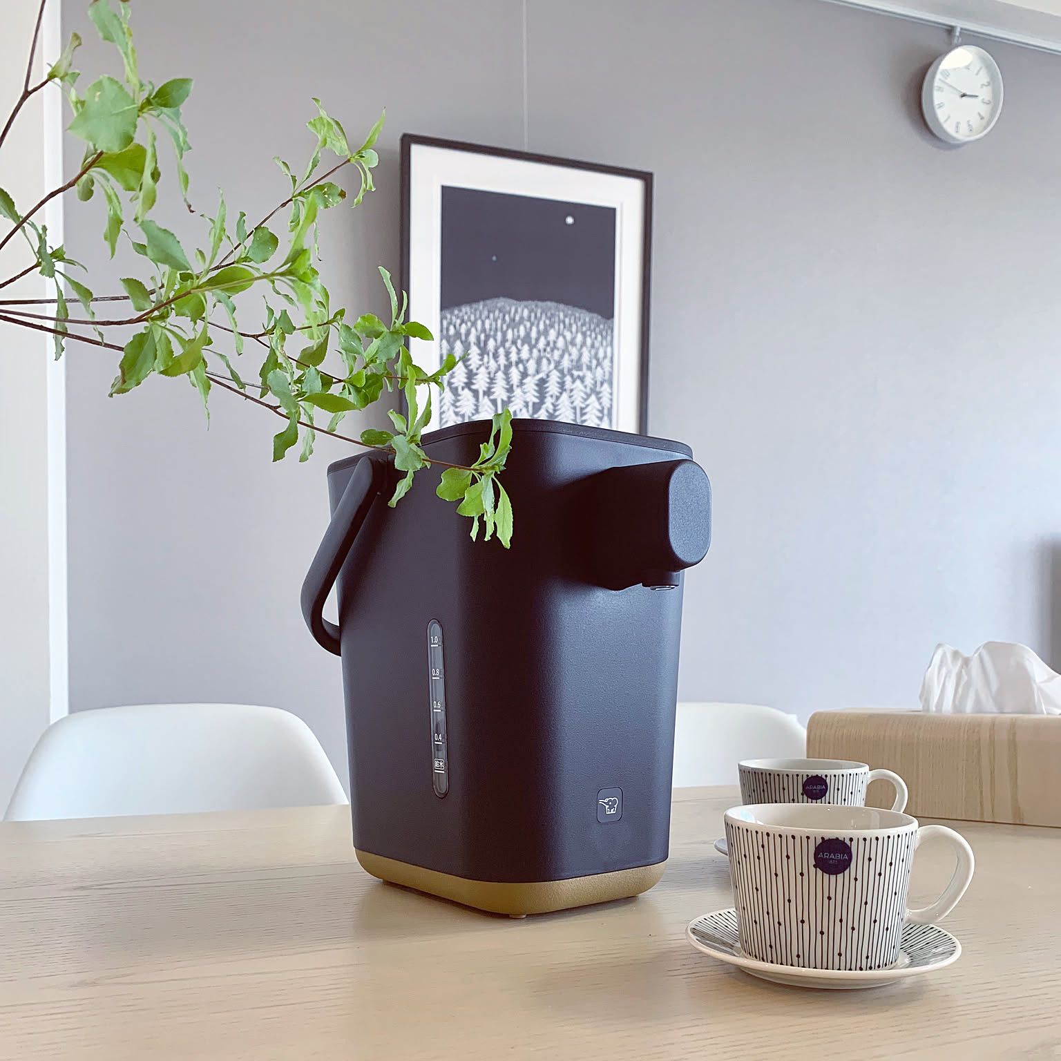 Compact black Zojirushi STAN water boiler on a dining table with two cups.