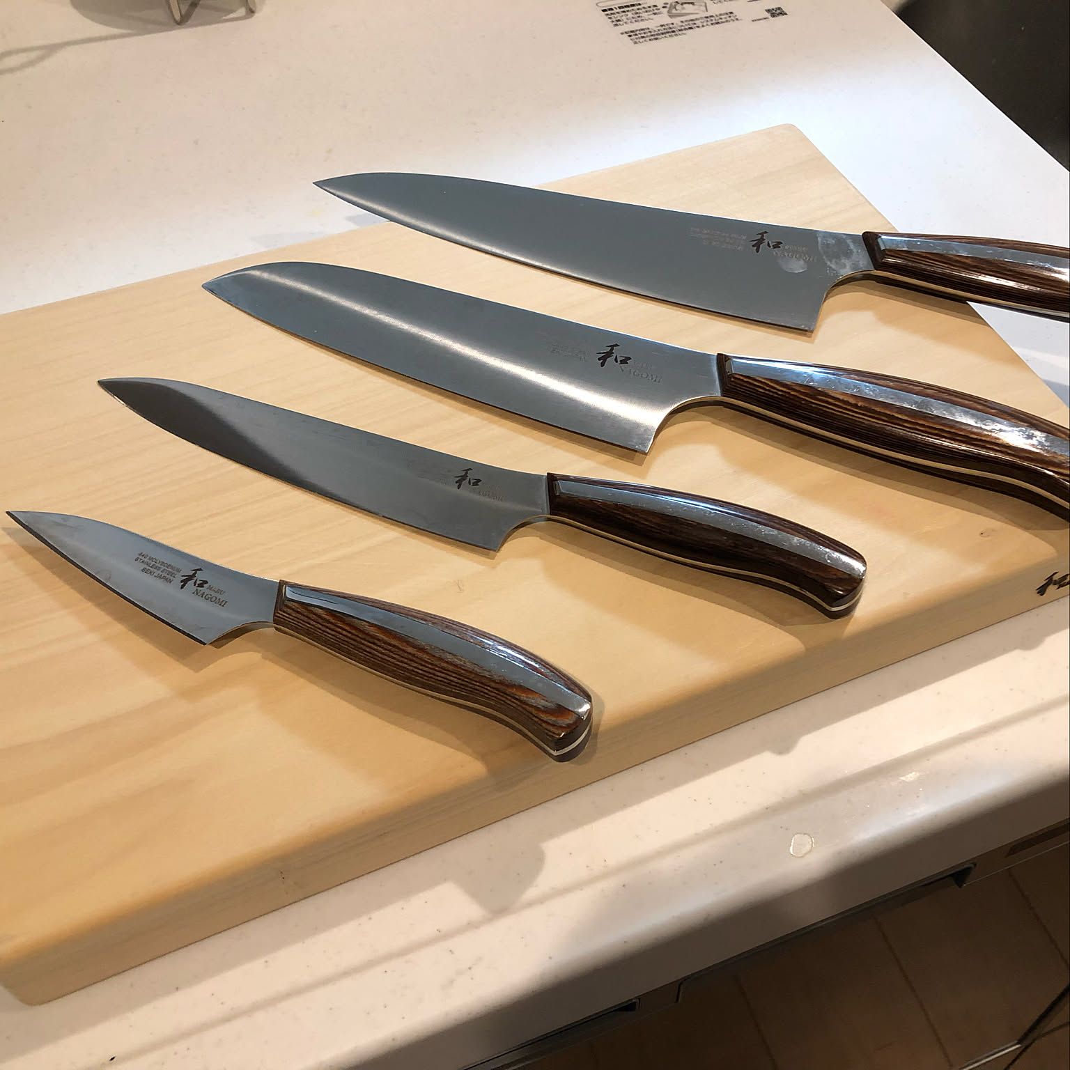 Japanese kitchen knives in several blade shapes arranged on a wooden cutting board.