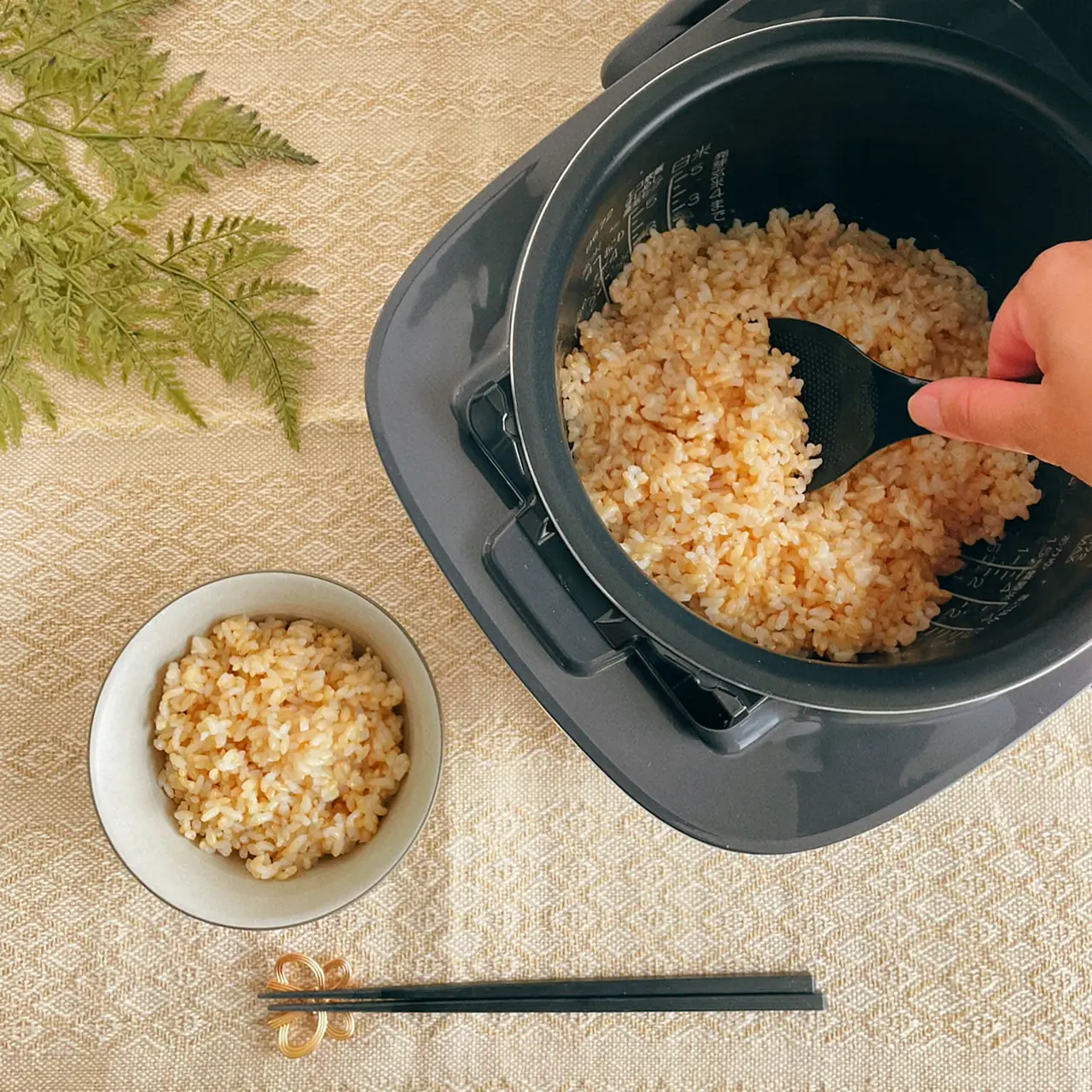 A black Zojirushi pressure IH rice cooker with cooked brown rice shown as part of a home cooking setup in a Japanese kitchen.