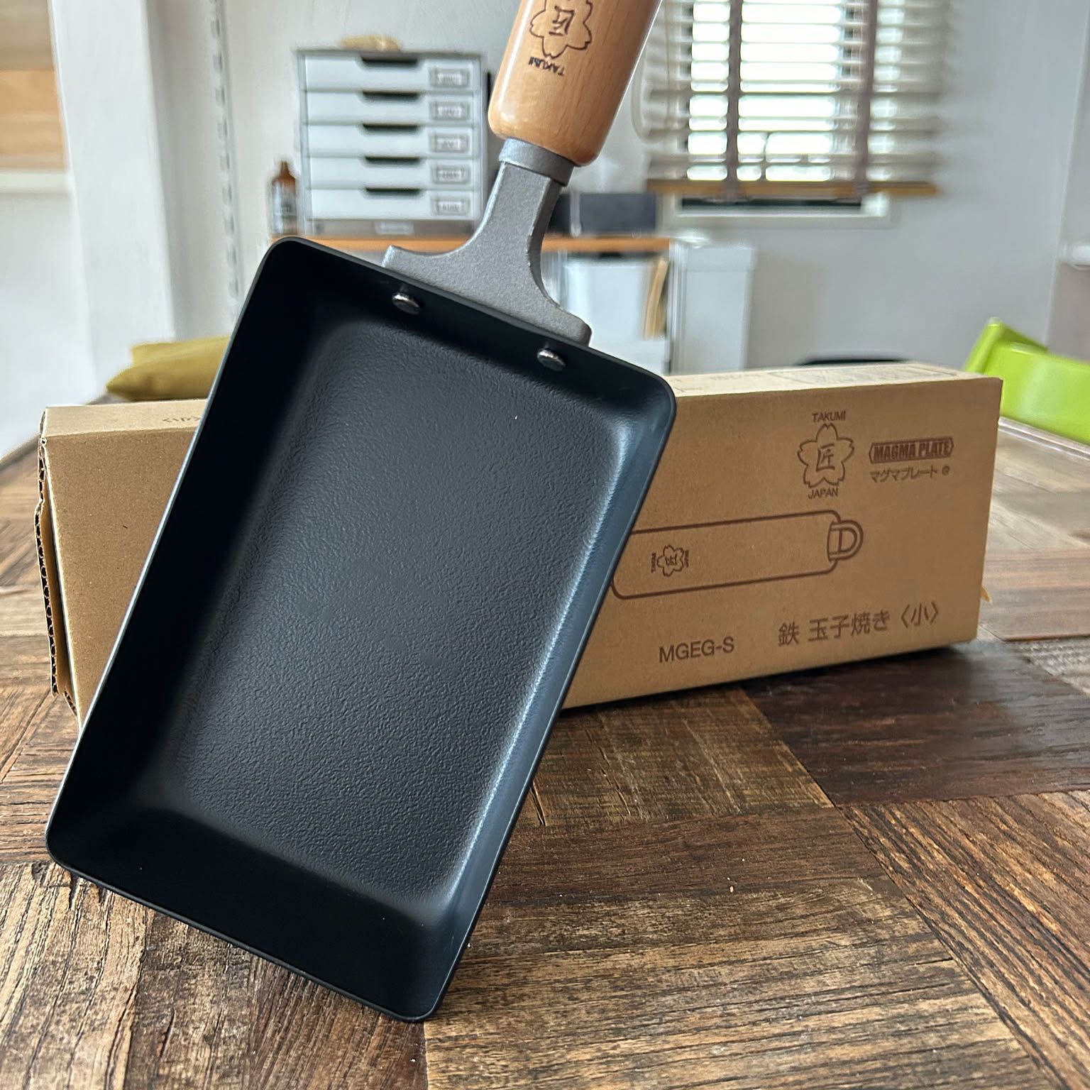 Compact rectangular Japanese iron tamagoyaki pan displayed in front of its box.