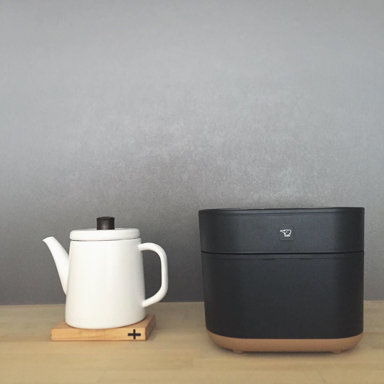 A matte-black Zojirushi STAN rice cooker with the Zojirushi bird logo, beside a white kettle on a wood counter