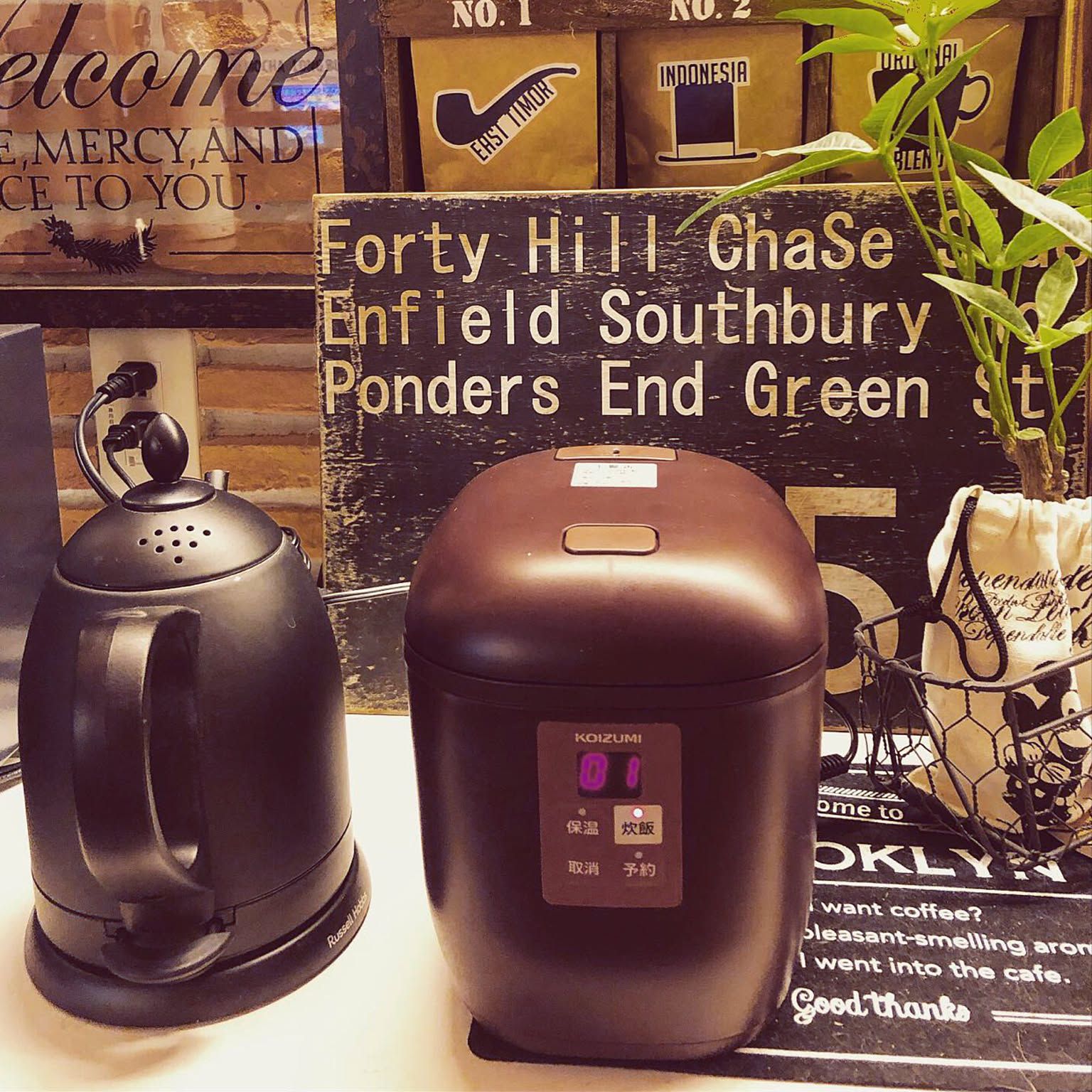 A compact brown Koizumi mini rice cooker beside an electric kettle in a cafe-style kitchen setup.