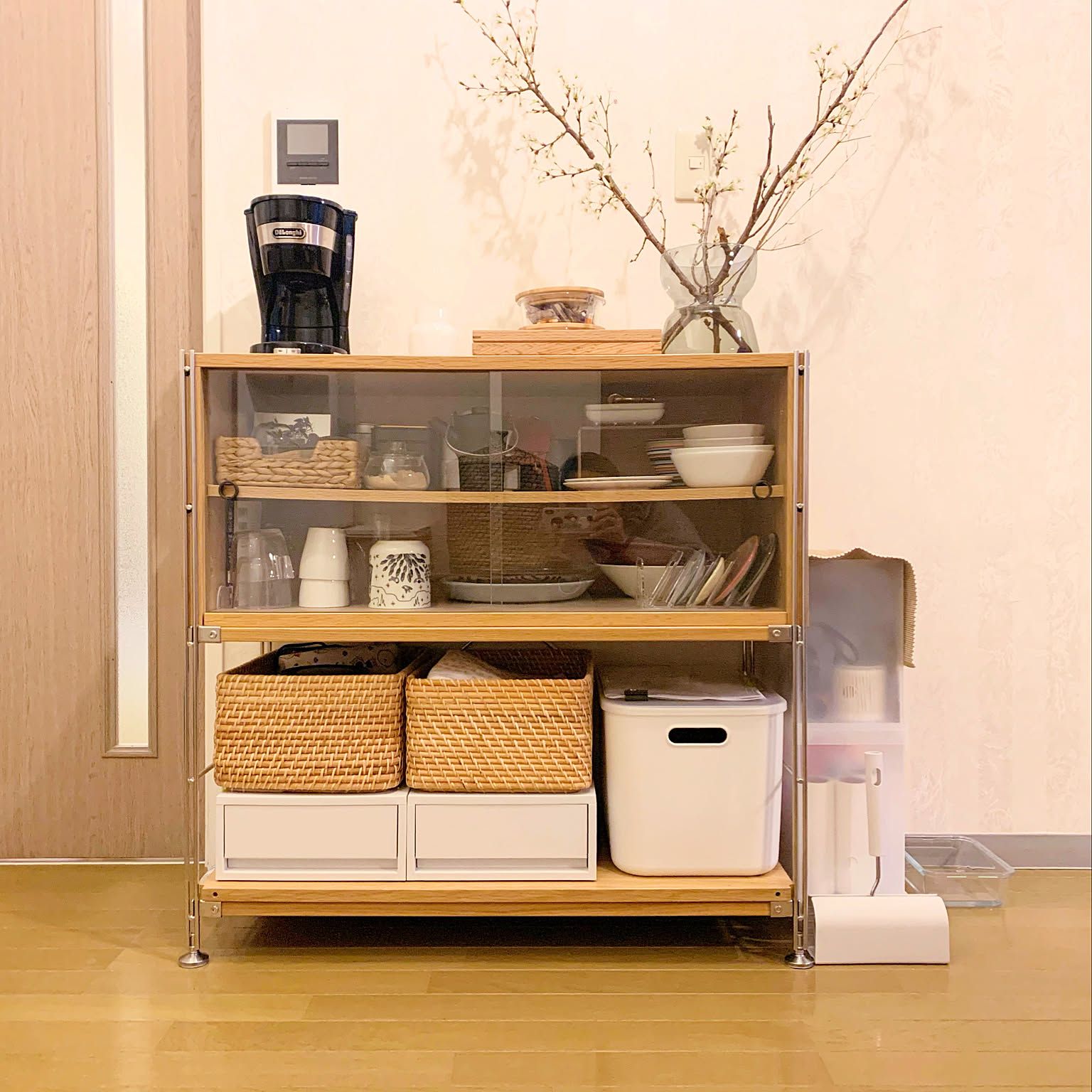 A MUJI unit shelf with an oak glass-door cabinet on top, two rattan baskets and a white soft polyethylene case on the lower shelf.