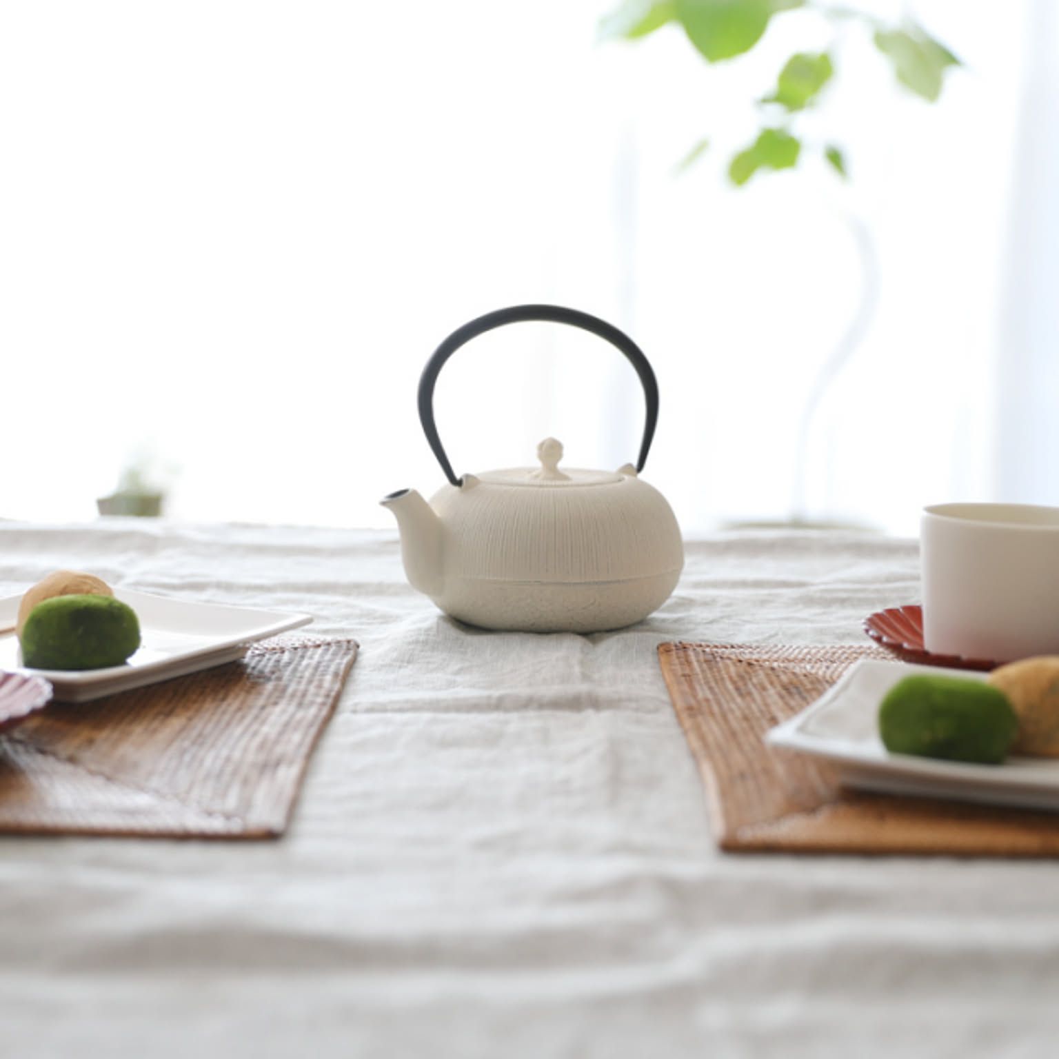 Cream and gold Nambu cast iron teapot on a linen tablecloth with wagashi sweets on small plates.