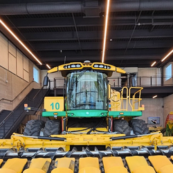 A massive harvester with a wide corn header is displayed inside a modern industrial building in Potage County, WI
