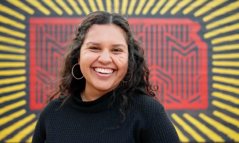 Smiling Salina, KS resident in front of the Love Salina mural Completed in 2022 by artist Eric Montoy at 125 S Santa Fe.