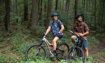 Two bikers smiling on a dirt path in the woods