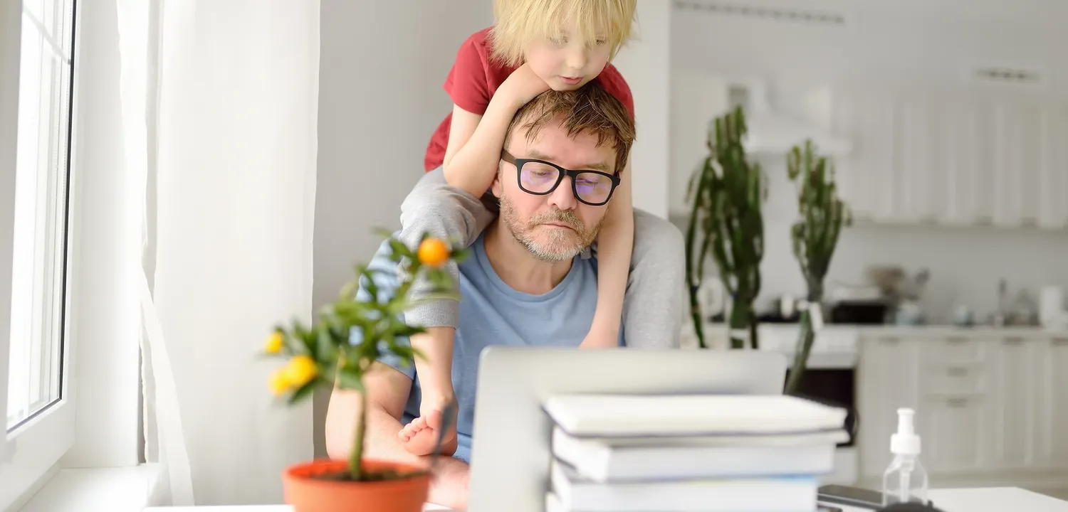 Man attempts to work from home with son on shoulders. 