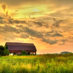 The sun sets over an old barn in a grassy field