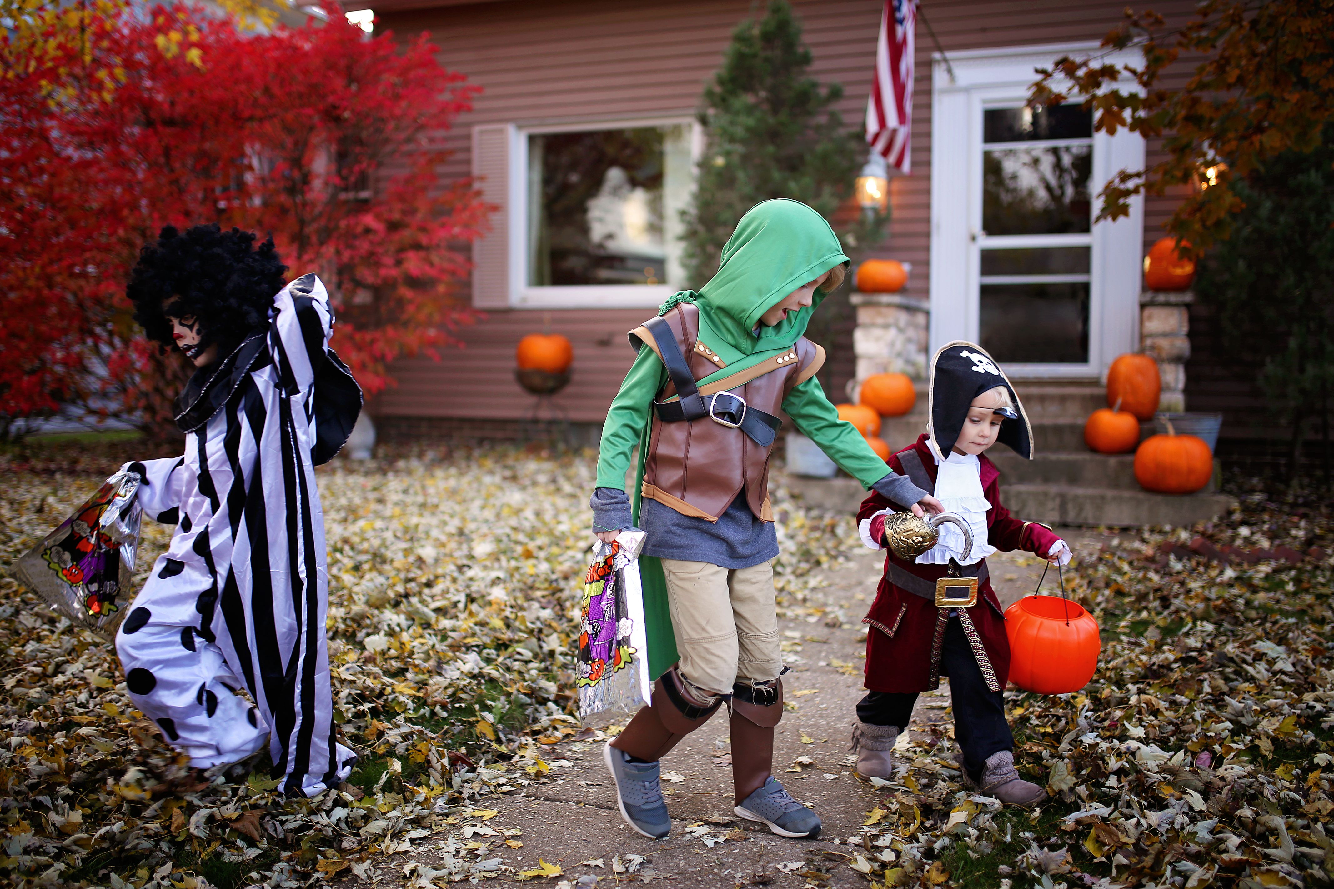 Three children stand on a lawn as they go trick or treating 