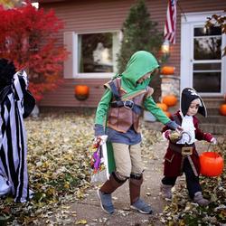 Three children stand on a lawn as they go trick or treating 