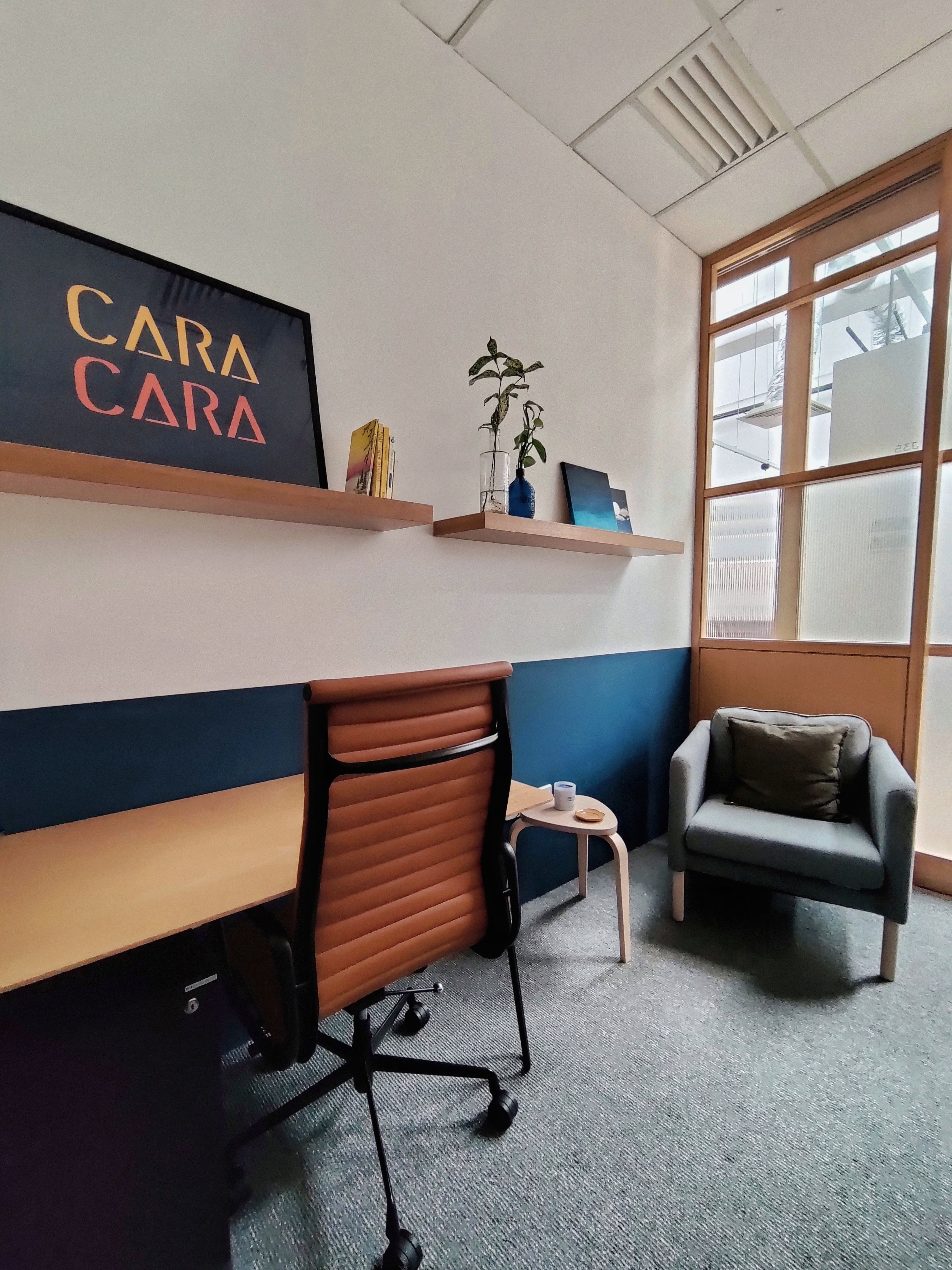 A therapy room at Cara Cara Jaya One with a desk, an armchair, and decorations on a wall shelf.