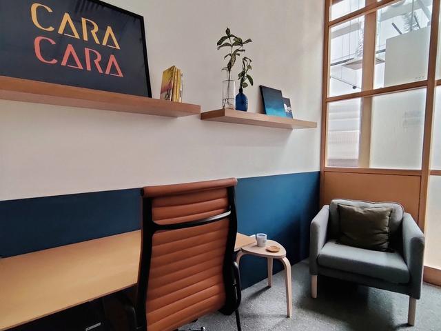 A therapy room at Cara Cara Jaya One with a desk, an armchair, and decorations on a wall shelf.