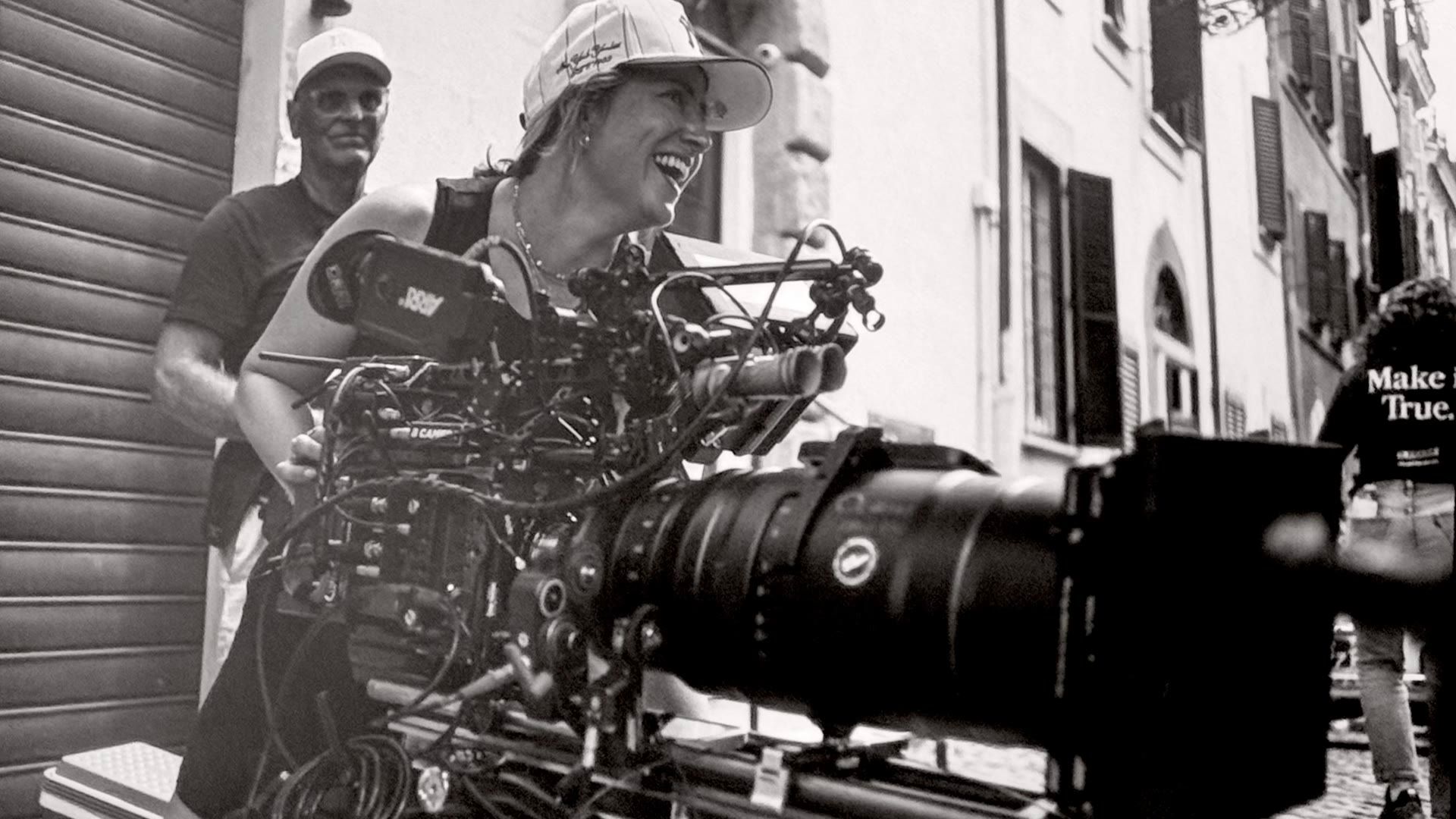 Angelia Hughes laughing while operating a camera rig on a narrow street.