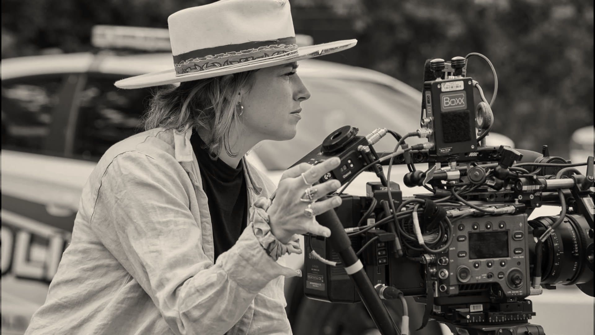 Angelia Hughes, in a wide-brimmed hat, operating a cinema camera on an exterior location.
