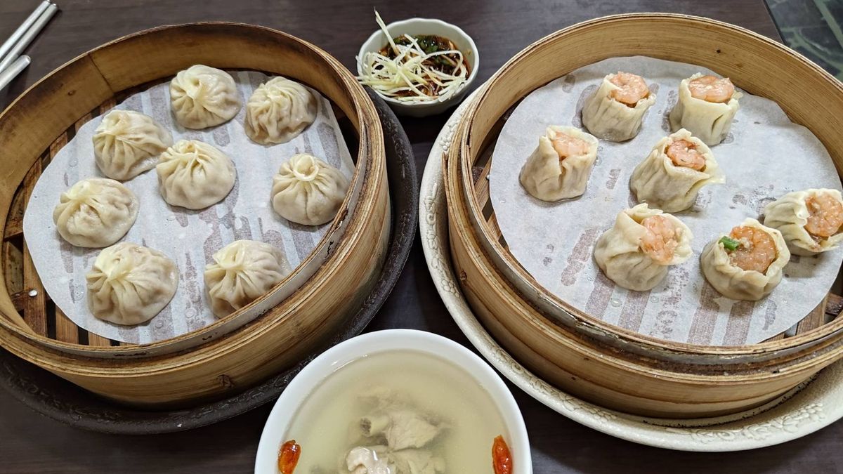 Two bamboo steamers of xiaolongbao and shrimp shao mai with a ginger-vinegar dip and a bowl of clear pork soup