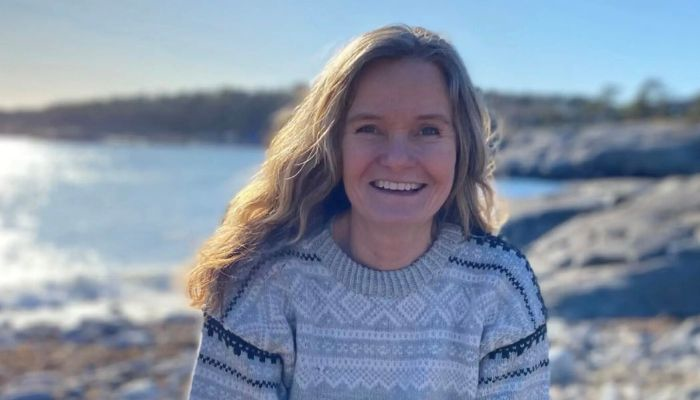 Kvinne i ullgenser ved sjøen.