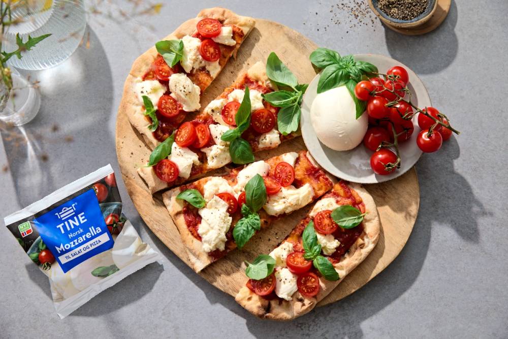 Pinsa Romana skiver med mozzarella, tomater og basilikum på et rundt trefjøl.