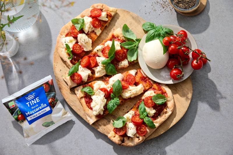 Pinsa Romana skiver med mozzarella, tomater og basilikum på et rundt trefjøl.