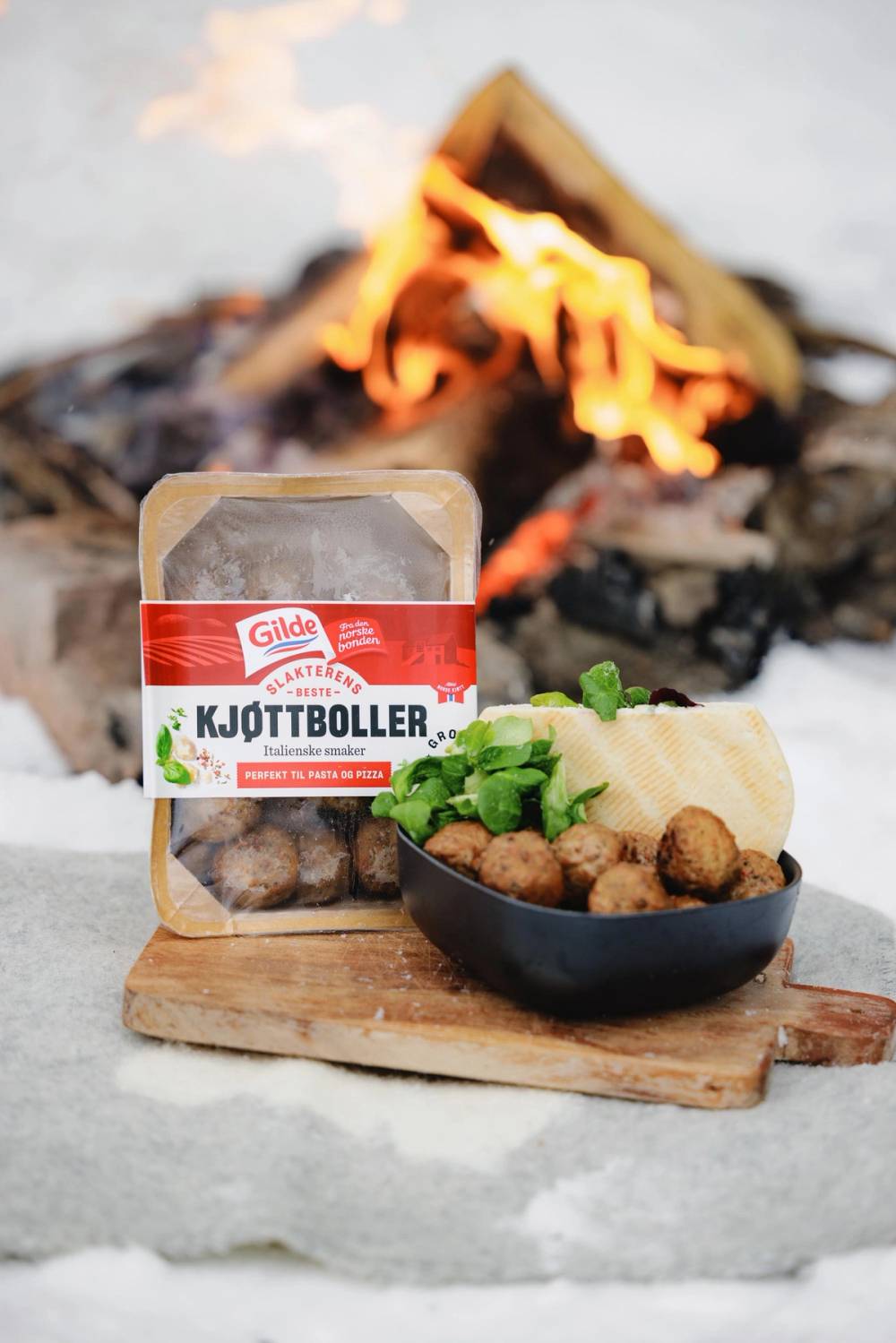 Kjøttboller og pitebrød med salat i skål på fjøl foran bål om vinteren.