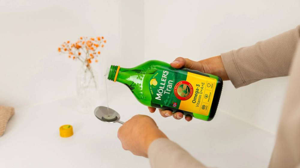 Person som heller Möllers Tran på en spiseskje.