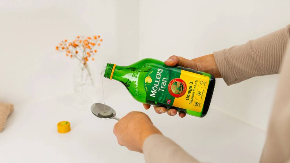 Person som heller Möllers Tran på en spiseskje.