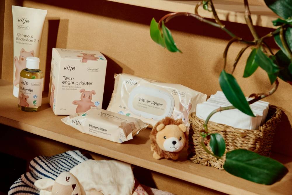Våtservietter, tørre engangskluter, babyolje og sjampo & badesåpe 2 i 1 fra Vilje i trehylle.