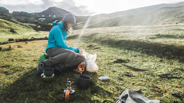 Kvinne som lager mat på primus på tur.