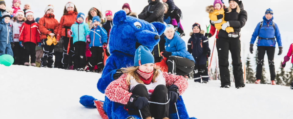 Barn som aker i akebakke og barn som ser på.