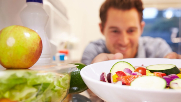 Mann som tar ut en skål med grønnsaker fra kjøleskapet.