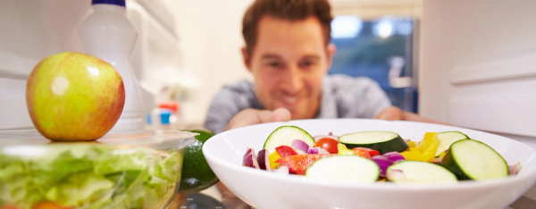 Mann som tar ut en skål med grønnsaker fra kjøleskapet.