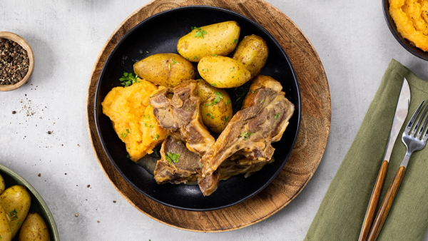 Pinnekjøtt, poteter og kålrotstappe på svart tallerken.