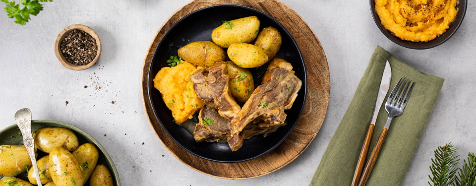 Pinnekjøtt, poteter og kålrotstappe på svart tallerken.