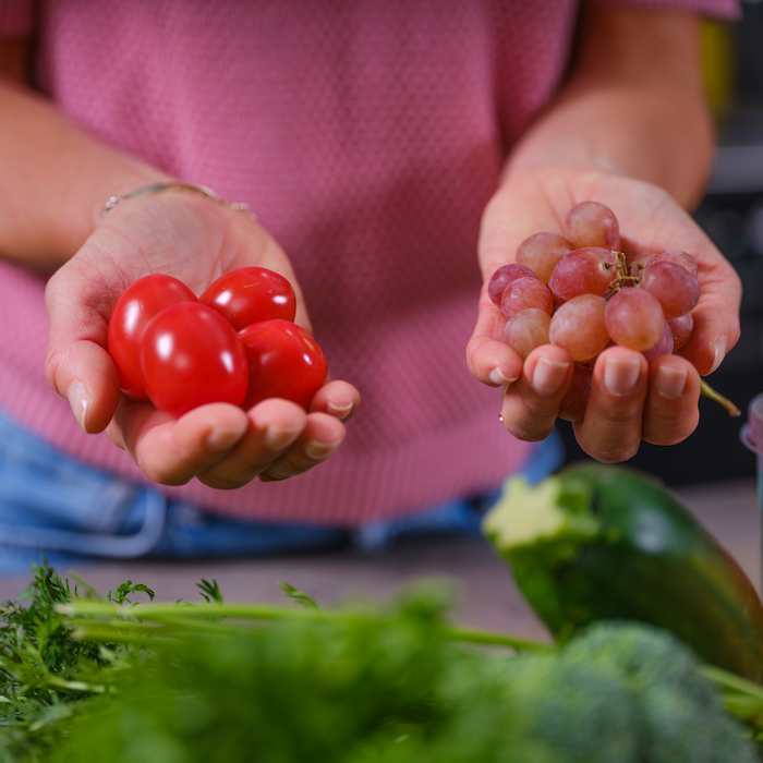 Hender som holder frem en porsjoner med frukt og grønt.