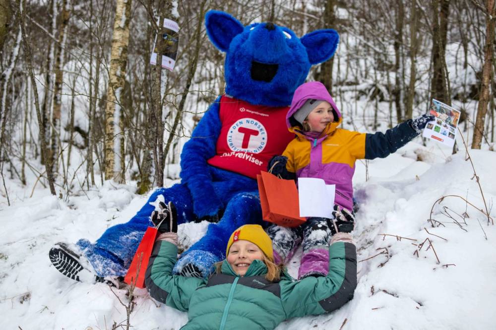 To barn og maskot som sitter i skogen på DNTs Kom deg ut dagen.