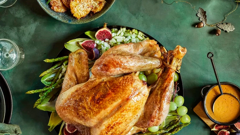 Hel kalkun servert på fat på bord med grønn duk pyntet for jul.