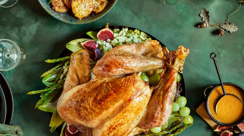 Hel kalkun servert på fat på bord med grønn duk pyntet for jul.