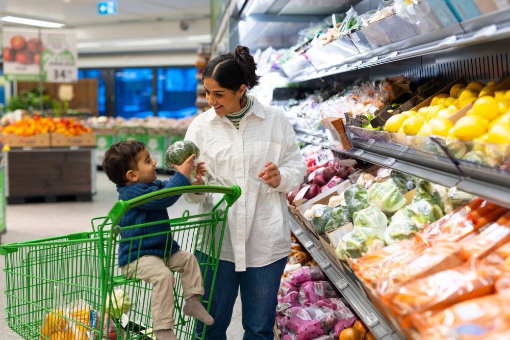 Mor og sønn som sitter i handlevognsetet i grønnsaksavdelingen hos KIWI.