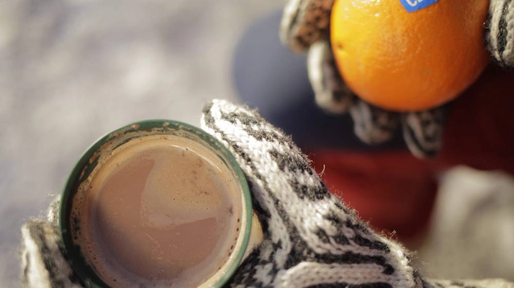 Hender med votter som holder en kopp med kakao og appelsin.