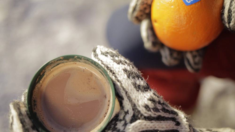 Hender med votter som holder en kopp med kakao og appelsin.