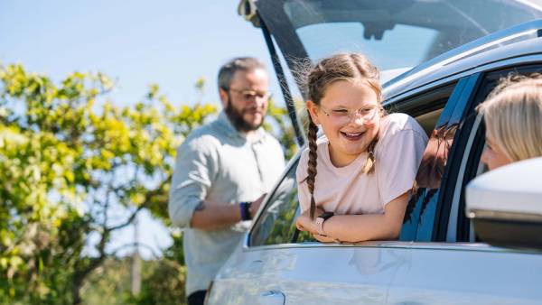 Familie som pakker bilen for bilferie hvor mor og barn ser ut av bilvinduene på hverandre.