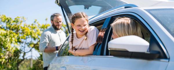 Familie som pakker bilen for bilferie hvor mor og barn ser ut av bilvinduene på hverandre.
