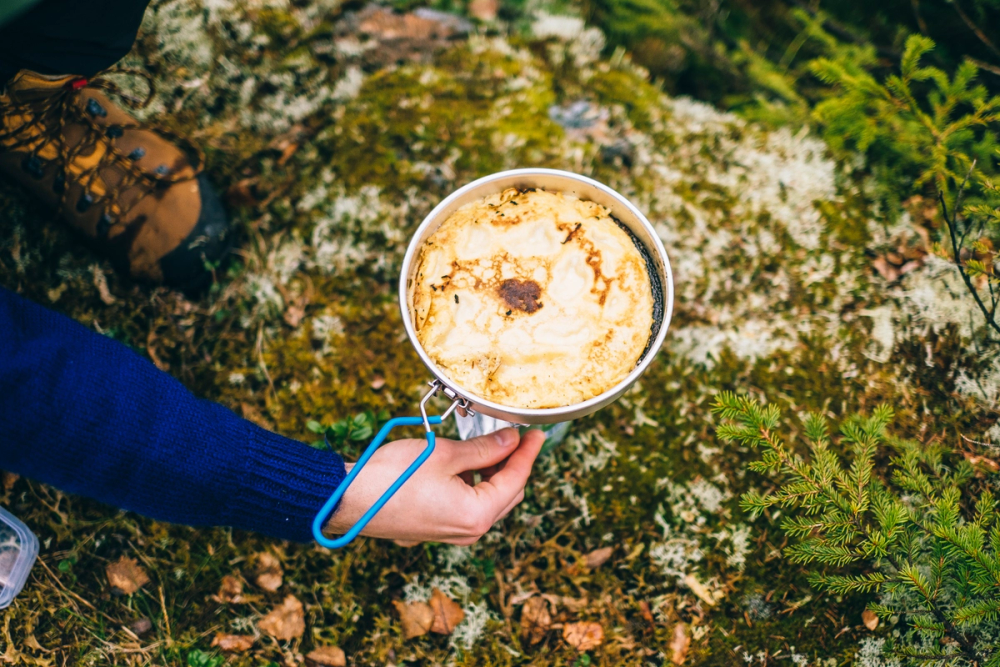 Primus med en pannekake, på en mosegrodd bakke i skogen.
