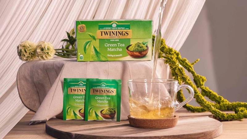 Grønn te helles i tekopp på et bord med Twinings green tea matcha-pakning