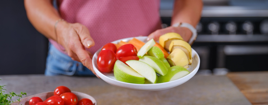 Hender som holder frem en skål med frukt og grønnsaker.