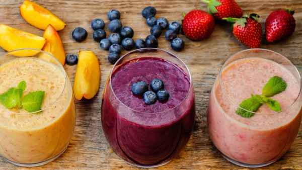 Grønn, gul, lilla og rosa smoothie i glass på rekke laget med bær, frukt og grønnsaker.