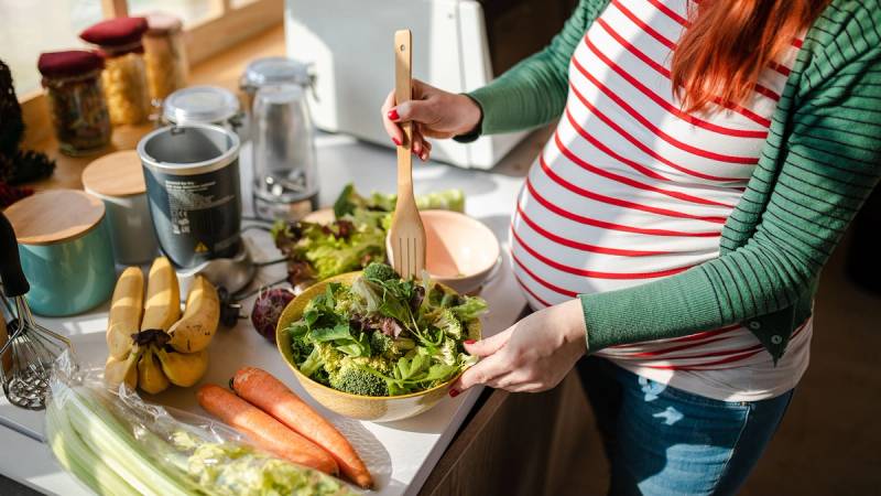 Gravid kvinne som lager salat til hverdagsmat.