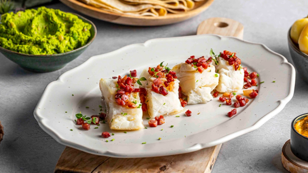 Lutefisk i porsjonsstykker med bacon på fat og skåler med ertepuré og poteter.