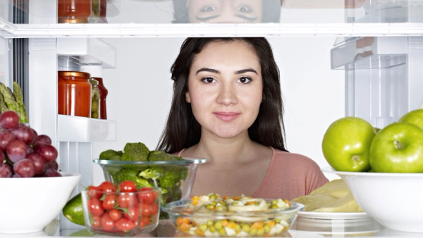 Kvinne som har åpnet dør i kjøleskap hvor det står frukt og grønnsaker.