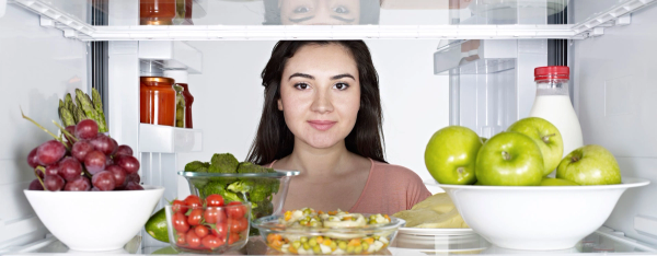 Kvinne som har åpnet dør i kjøleskap hvor det står frukt og grønnsaker.